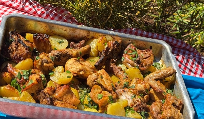 Frango assado dourado com batatas em rodelas levemente crocantes nas bordas, tudo coberto com cebolas caramelizadas e cheiro-verde fresco. Servido em assadeira rústica sobre mesa de madeira.