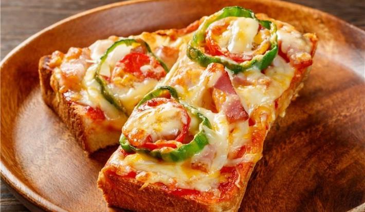 Fotografia de um pão pizza de queijo deretido com tomate, cortado na metade e a outra metade esta apoiado sobre a outra metade. As metades estão em um prato redondo de madeira raso.