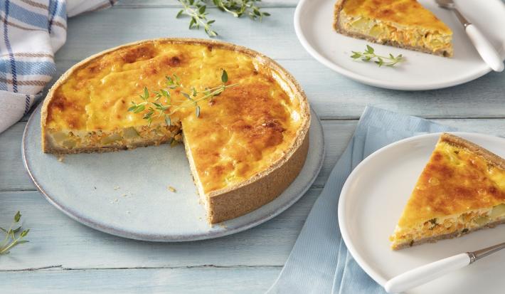 Foto em tons de branco da receita de torta de legumes com iogurte natural servida em uma porção grande sobre uma base de cerâmica com duas fatias ao lado sobre pratos menores