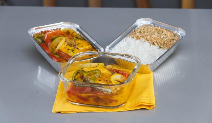 Foto da receita de Moqueca de Peixe Maggi, em um recipiente de vidro e alumínio, sobre um pano amarelo, em uma bancada