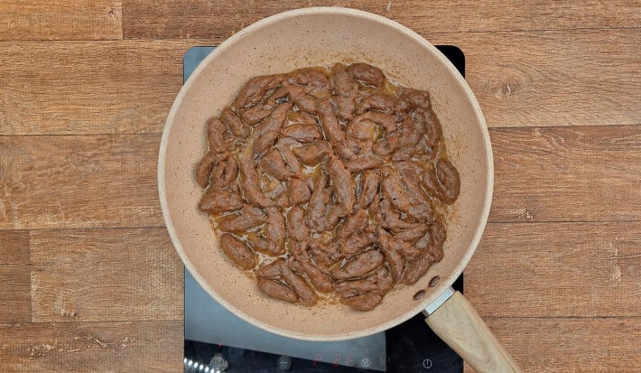 Carne em tiras cozida com caldo de carne na frigideira.