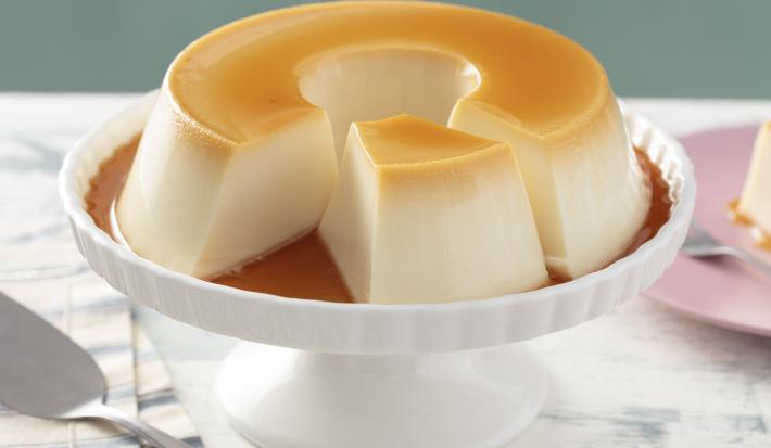 Imagem de uma boleira branca com o pudim de gelatina cortado com uma fatia separada.
