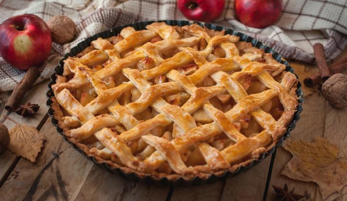 Imagem de uma torta de maçã trançada bem dourada com maçãs ao redor.
