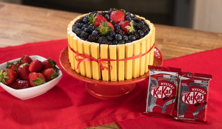 Fotografia em tons de vermelho com um bolo decorado com KitKat mystery, o biscoito kitkat de cor amarela. O bolo possui diversas frutas vermelhas no topo. Fotografia em tons de vermelho com um bolo decorado com KitKat mystery, o biscoito kitkat de cor amarela. O bolo possui diversas frutas vermelhas no topo.