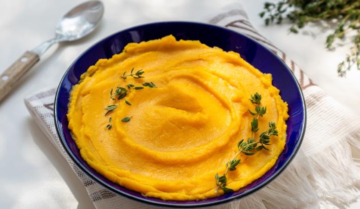fotografia em tons de laranja, branco e azul de uma mesa branca. Contém um recipiente azul com o purê de abóbora dentro.