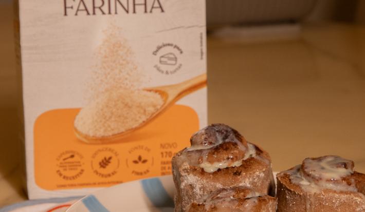 Fotografia em tons de amarelo em uma bancada com um prato azul ao centro e três cinnamon rolls em cima. Ao fundo, uma embalagem de nestlé farinha de aveia.