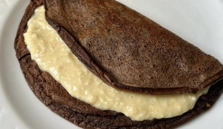 Fotografia de uma panqueca de chocolate com recheio de coco cremoso sobre um prato branco de vidro.