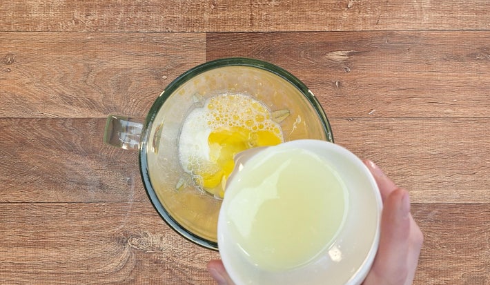 Mão despejando suco de limão dentro de liquidificador com ovos e leite.
