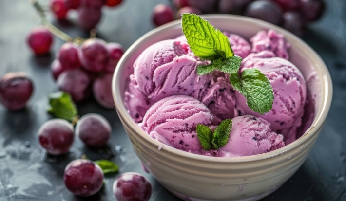 Fotografia em tons de roxo com um pote de sorvete ao centro. Dentro do pote existe uma receita de sorvete de uva de cor roxa finalizado com ramos de hortelã Fotografia em tons de roxo com um pote de sorvete ao centro. Dentro do pote existe uma receita de sorvete de uva de cor roxa finalizado com ramos de hortelã