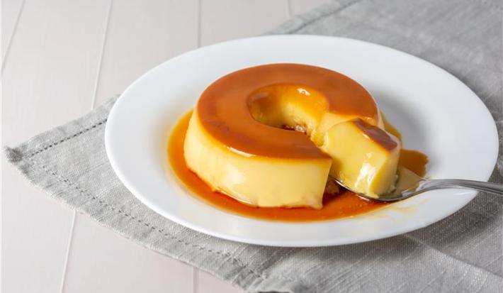 Foto de pudim disposto em um prato branco cortado com uma colher
