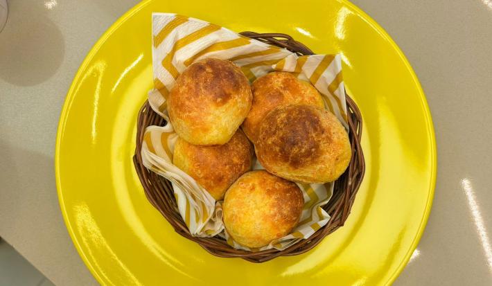 Fotografia em tons de amarelo com um prato amarelo ao centro. Dentro do prato existe uma cestinha com vários pãezinhos feito com queijo e Ninho Adulto