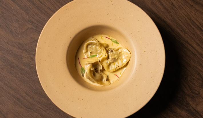 Foto da receita de Ravioli de Escargot feito no Masterchef 11. Observa-se um prato fundo visto de cima com três raviolis servidos com molho e decorado com brotos.