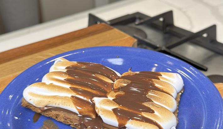 Fotografia de uma receita de smores com cookie em um prato de vidro raso sobre uma tábau de madeira.