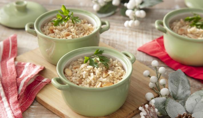 Foto da receita de arroz integral com amêndoas servida em três panelinhas verdes sobre uma tábua de madeira em cima de uma mesa decorada com elementos de inverno