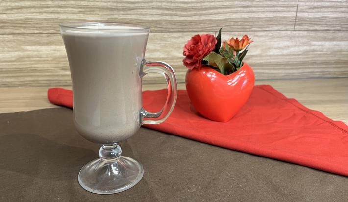 Fotografia em tons de vermelho e marrom com uma caneca de vidro ao centro. Dentro da caneca existe uma receita de Choco-mate Cremoso feito com chá mate e achocolatado NESCAU Extra Cacau 30%