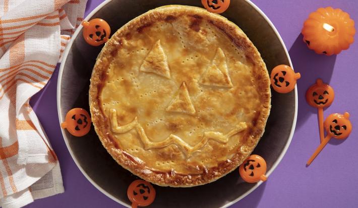 Foto da receita de Torta Folhada Cremosa de Frango com Abóbora para o Dia das Bruxas servida em um prato grande preto com decoração de halloween em volta