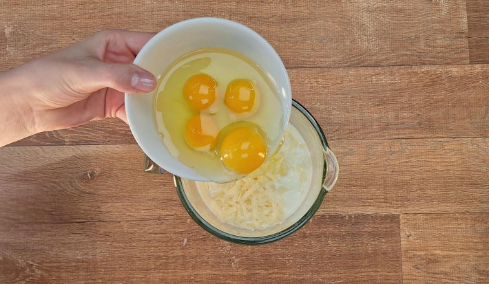 Ovos sendo despejados dentro de liquidificado com leite e queijo parmesão visíveis.