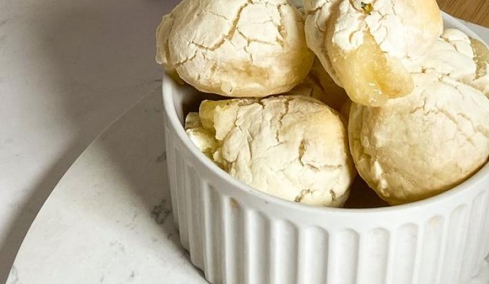 Foto da receita de pão de queijo vegano servida em diversas porções em um prato de porcelana branca sobre uma tábua de madeira.