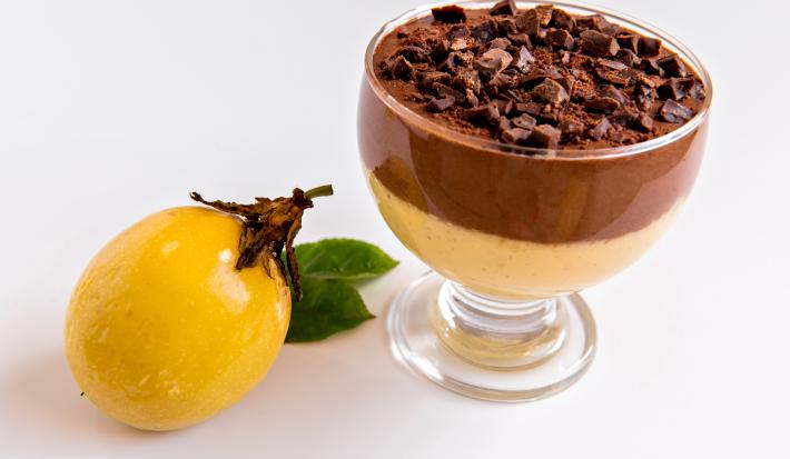 Receita de Mousse de Maracujá com Chocolate, fácil e delicioso, feito com Leite MOÇA, suco e maracujá concentrado, NESTLÉ Creme de Leite e Chocolate ao Leite NESTLÉ CLASSIC, servido em uma taça ao lado de uma maracujá