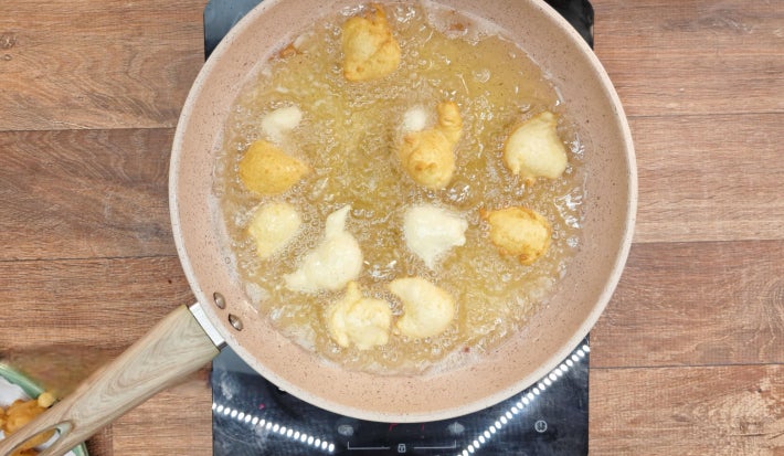 Bolinhos de chuva fritando em óleo quente dentro de frigideira sobre fogão portátil preto.