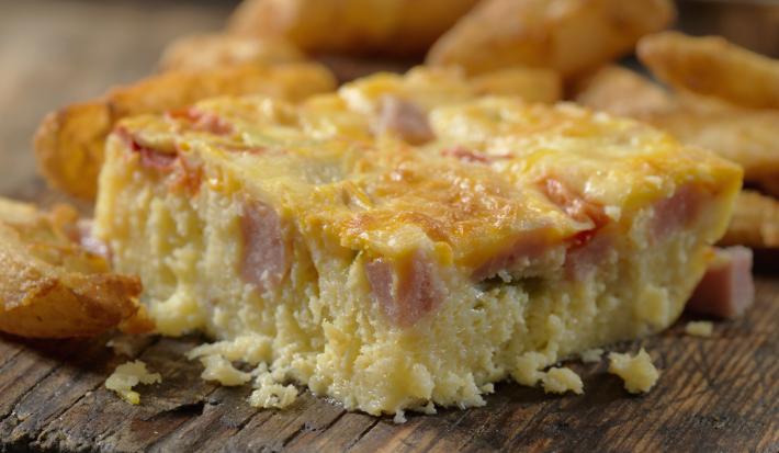 Fotografia de uma torta de panqueca recheada cortada em pedaços, sobre uma tábua de madeira.