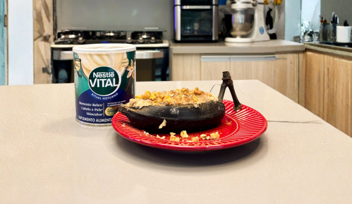 Fotografia em tons de verde e azul em uma bancada de cozinha com um prato vermelho e uma banana assada em cima dele.