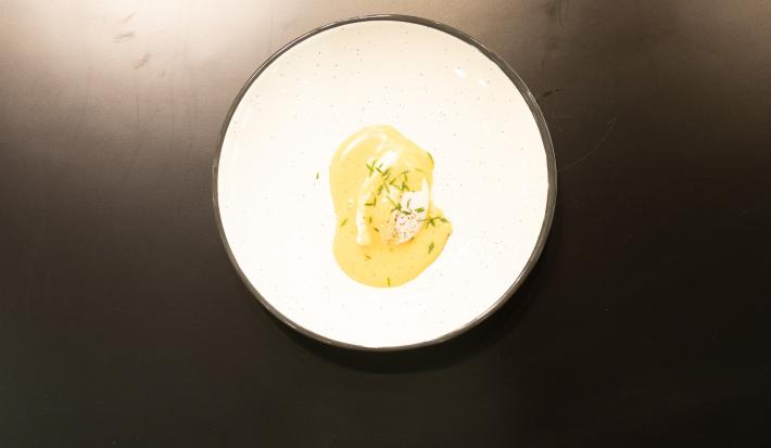 Fotografia vista de cima de uma bancada preta com um prato branco. Dentro do prato tem uma receita de ovo pochê com hollandaise e ciboulette.