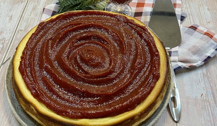 Foto da Receita de Torta de Ricota com Goiabada. Observa-se uma torta inteira com uma espátula prateada ao lado direito em cima de uma tábua de madeira clara.