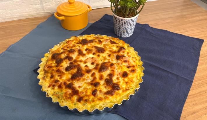 Fotografia em tons de azul com uma forma ao centro. Dentro da forma existe uma receita de quiche com massa de batata gratinada.
