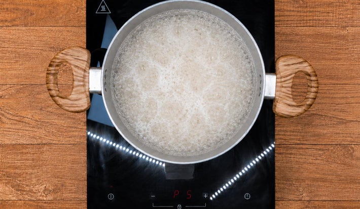 Arroz em água fervente em panela sobre fogão portátil preto