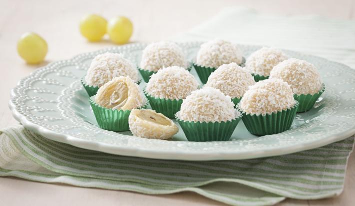 Fotografia em tons de verde e branco de uma bancada vista de frente, contém um pano listrado em verde e branco, um prato redondo branco com vários beijinhos em forma de bolinha com coco por cima. Fotografia em tons de verde e branco de uma bancada vista de frente, contém um pano listrado em verde e branco, um prato redondo branco com vários beijinhos em forma de bolinha com coco por cima.