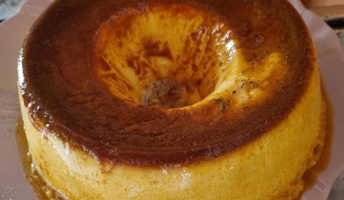 Fotografia de um pudim de maracujá com calda de caramelo de leite escorrendo sobre um apoio branco.