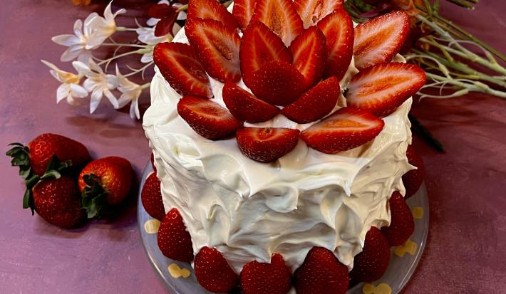 Receita de Bolo Confeitado com Chantininho. Observa-se um bolo alto coberto com chantinho e decorado com morangos.