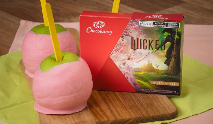 Imagem de duas maçãs do amor cobertas com chocolate rosa. Ao lado, uma caixinha do chocolate Wicked.