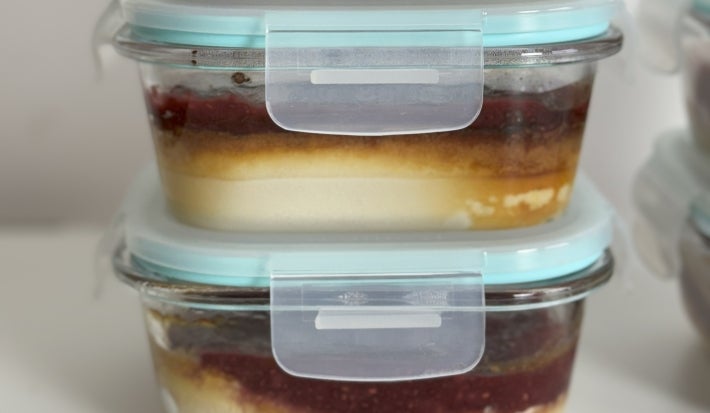 Fotografia de três recipientes de vidro com tampa, um sobre o outro, em uma mesa branca. Dentro dos recipientes tem uma receita de cheesecake.