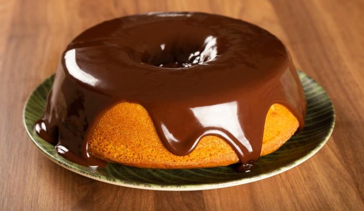 Foto da receita de Bolo de Cenoura. Observa-se o bolo em um prato de porcelana com calda de chocolate por cima escorregando.