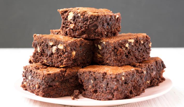 Imagem de um prato rosa claro com pedaços quadrados de brownie empilhados.