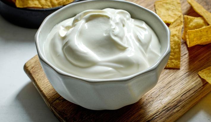 Imagem de um bowl branco com requeijão cremoso e nachos ao lado.
