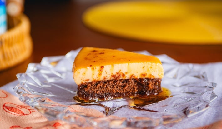 Fotografia mostra uma fatia do bolo pudim, onde são visíveis as camadas de bolo de chocolate e pudim.