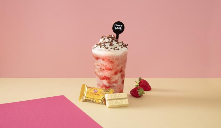Foto em tons de cor de rosa da receita de smoothie de morango servida sobre uma mesa amarela com kit kat amarelo à frente