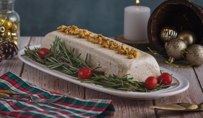 Foto da receita de Mousse de Queijos, num prato branco, sobre uma bancada de madeira toda decorada com motivos natalinos, uma vez branca acesa ao fundo e um tecido colorido de natal como guardanapo