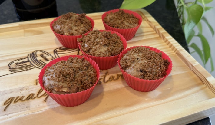 Foto da receita do Muffin de Maçã com Biscoito Tostines Especiarias Ginger, servidos em cinco forminhas vermelhas, sobre uma tábua de madeira