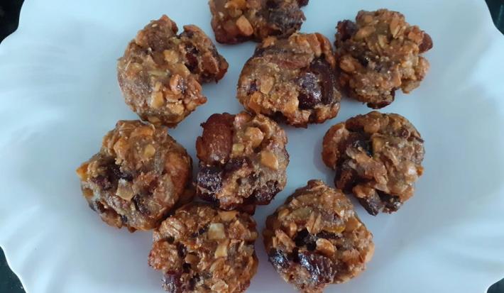 Foto em tons de marrom da receita de cookies de frutas secas e mucilon servida em diversas porções sobre um prato de porcelana branco