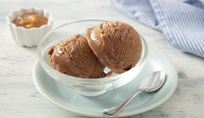 Foto da receita de MOÇA Sorvete de Doce de Leite. Observa-se um potinho individual de vidro com duas bolas de sorvete e, atrás, um potinho com doce de leite cremoso.