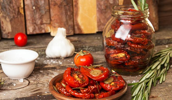 Fotografia em tons de marrom com um pote de vidro ao centro. Dentro do pote existe uma receita de tomate seco feita na Air Fryer