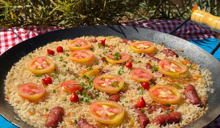 Fotografia de um tacho de ferro fundo com uma receita de arroz com calabresa decorada com tomate em rodelas e pimenta biquinho.