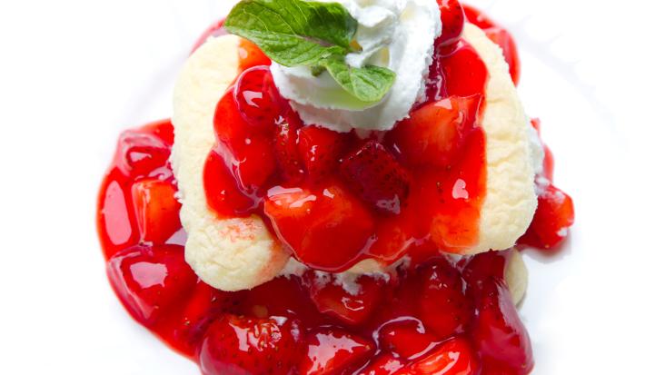 Fotografia em tons claros de uma receita de cremoso de baunilha com frutas vermelhas sobre um apoio branco.