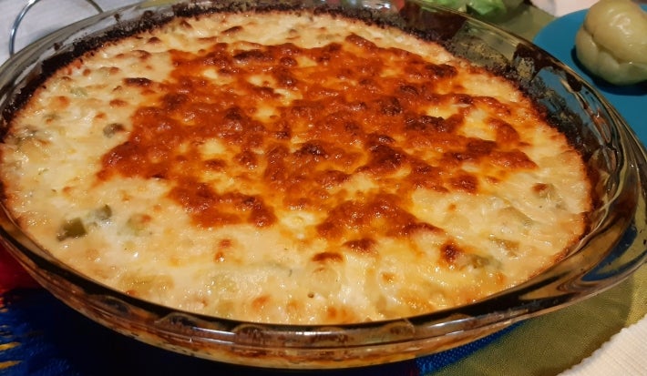 Um recipiente de vidro transparente apresenta um queijo gratinado dourado, com uma crosta crocante.