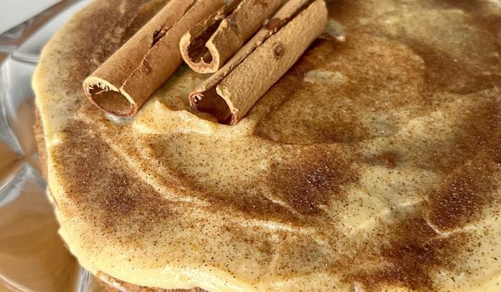 Fotografia mostra um bolo com cobertura de creme claro, polvilhado com canela.