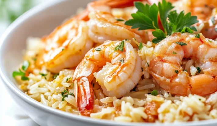 Prato branco com porção de arroz cremoso e camarão, decorado com uma folha de coentro.